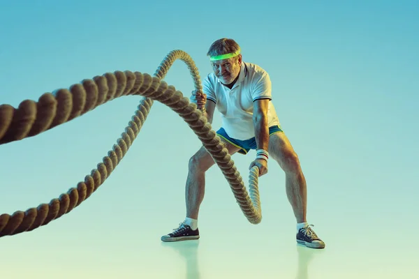 Senior man training met touwen in sportschoeisel op gradiënt achtergrond en neon licht — Stockfoto