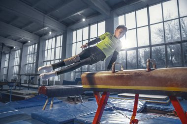 Spor salonunda küçük bir erkek jimnastikçi, esnek ve aktif.