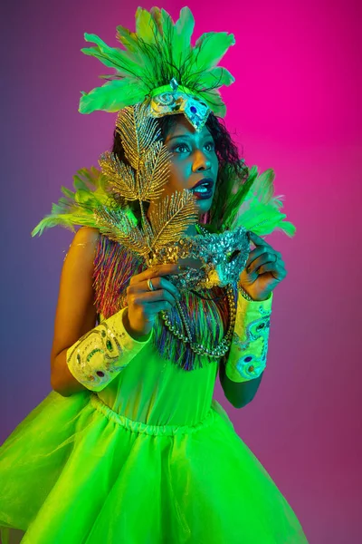 Mooie jonge vrouw in carnaval en maskerade kostuum op gradiënt studio achtergrond in neon licht — Stockfoto