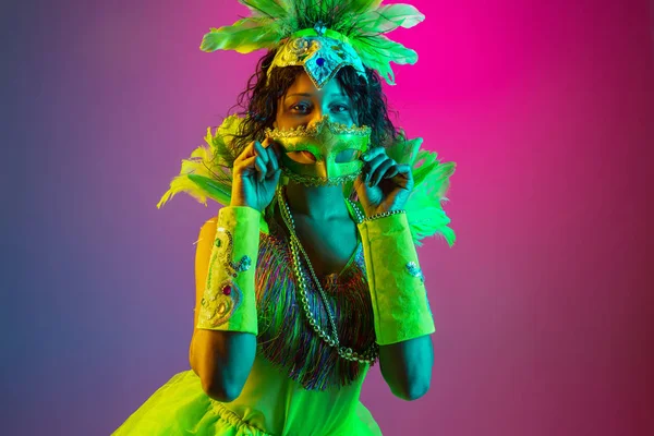 Mooie jonge vrouw in carnaval en maskerade kostuum op gradiënt studio achtergrond in neon licht — Stockfoto