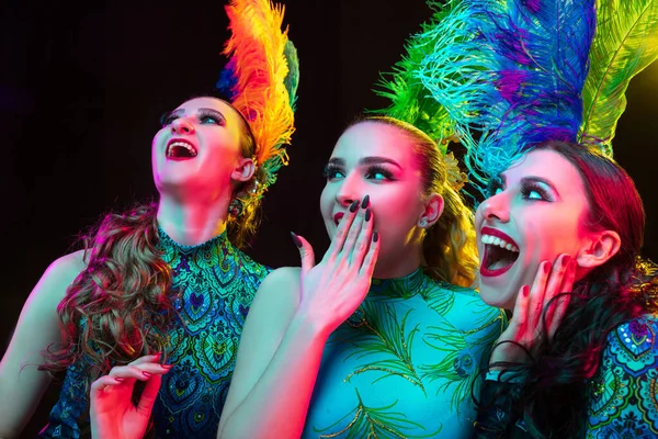 Hermosas mujeres jóvenes en carnaval y disfraz de mascarada en luces de neón de colores sobre fondo negro —  Fotos de Stock