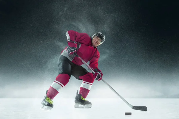 Male hockey player with the stick on ice court and dark background — Stock Photo, Image