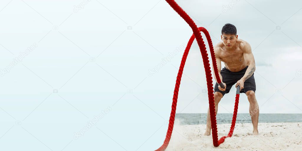 Young healthy man athlete doing exercise at the beach with ropes, flyer with copyspace