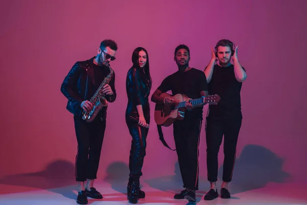 Gruppe junger multiethnischer Musiker gründete Band, die im Neonlicht auf rosa Hintergrund tanzte — Stockfoto