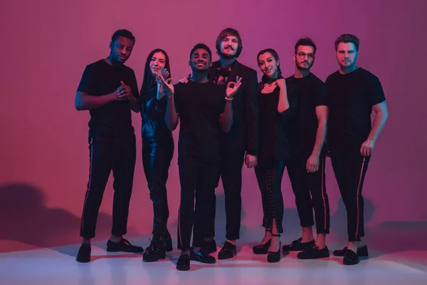 Fiatal, többnemzetiségű zenészek csoportja zenekart hozott létre, neon fényben táncolva rózsaszín háttérrel — Stock Fotó
