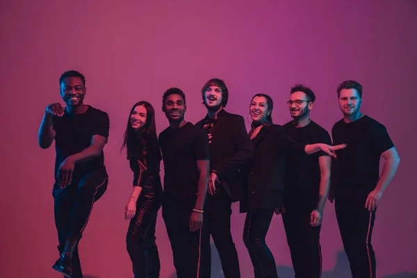 Genç çok ırklı müzisyenlerden oluşan bir grup, pembe arka planda neon ışıkta dans ederek grup kurdu. — Stok fotoğraf