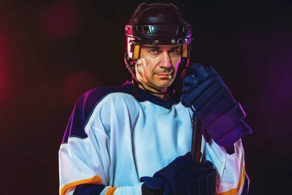 Jugador de hockey masculino con el palo en la pista de hielo y fondo de color neón oscuro — Foto de Stock