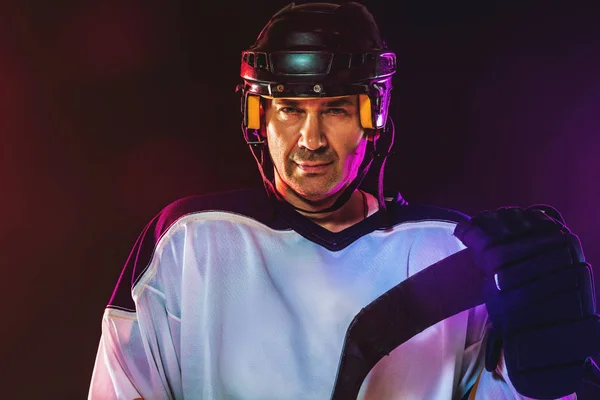 Hockeyspieler mit Stock auf dem Eis und dunklem neonfarbenen Hintergrund — Stockfoto