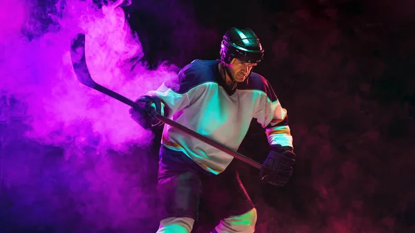 Jugador de hockey masculino con el palo en la pista de hielo y fondo de color neón oscuro — Foto de Stock