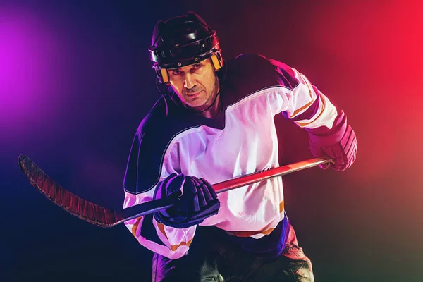 Pemain hoki pria dengan tongkat di lapangan es dan latar belakang berwarna neon gelap — Stok Foto