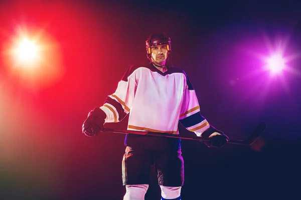 Hockeyspieler mit Stock auf dem Eis und dunklem neonfarbenen Hintergrund — Stockfoto