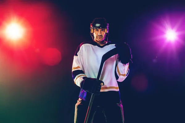 Hockeyspieler mit Stock auf dem Eis und dunklem neonfarbenen Hintergrund — Stockfoto