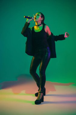Caucasian female singer portrait isolated on green studio background in neon light