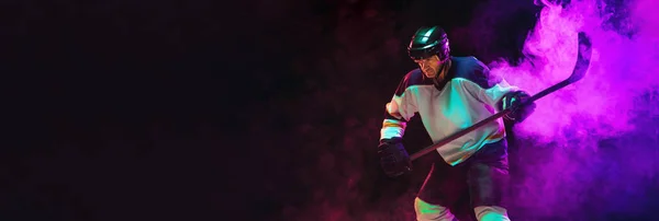 Male hockey player with the stick on ice court and dark neon colored background — Stock Photo, Image