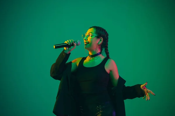 Retrato femenino de cantante caucásica aislado en fondo de estudio verde en luz de neón — Foto de Stock