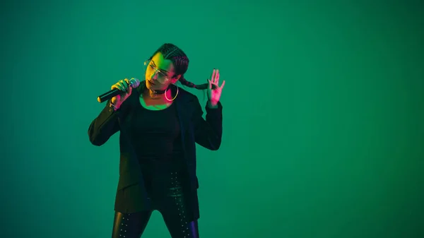 Retrato femenino de cantante caucásica aislado en fondo de estudio verde en luz de neón —  Fotos de Stock