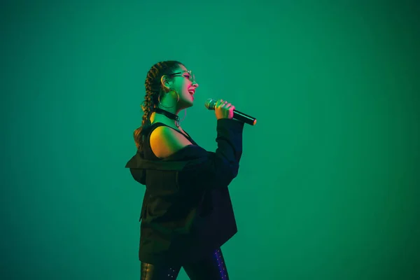 Caucasian female singer portrait isolated on green studio background in neon light — 图库照片