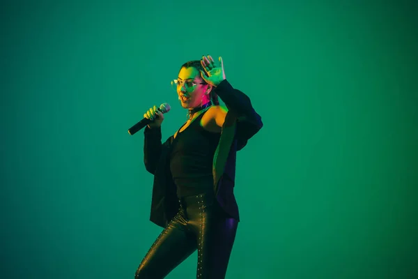 Caucasian female singer portrait isolated on green studio background in neon light — стокове фото