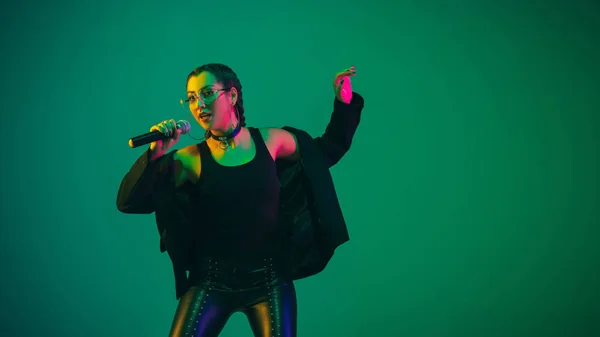 Caucasian female singer portrait isolated on green studio background in neon light — Zdjęcie stockowe