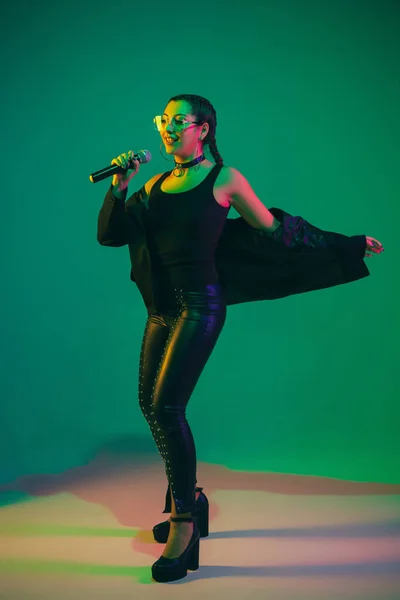 Caucasian female singer portrait isolated on green studio background in neon light — Zdjęcie stockowe