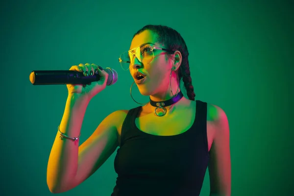 Caucasian female singer portrait isolated on green studio background in neon light — Stockfoto