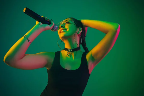 Caucasian female singer portrait isolated on green studio background in neon light — Stockfoto