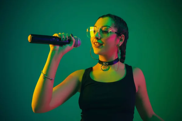 Caucasian female singer portrait isolated on green studio background in neon light — Stockfoto