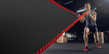 Genç sağlıklı erkek sporcu salonda iplerle, kopyalanmış alanla egzersiz yapıyor.