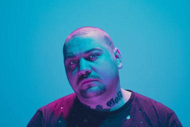 Portrait of a hipster guy with colorful neon light on blue background