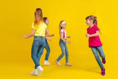 Happy children playing and having fun together on yellow studio background
