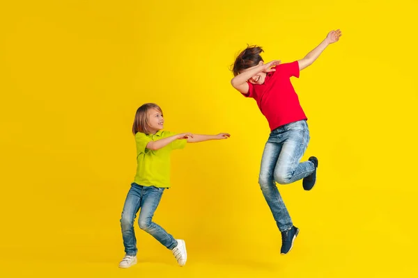 Happy children playing and having fun together on yellow studio background — 스톡 사진
