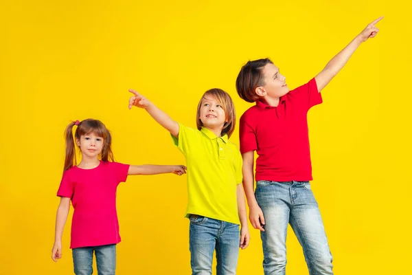 Niños felices jugando y divirtiéndose juntos en el fondo amarillo del estudio — Foto de Stock