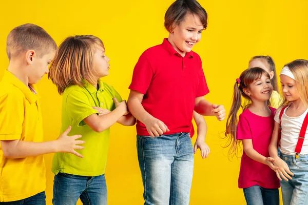 Niños felices jugando y divirtiéndose juntos en el fondo amarillo del estudio —  Fotos de Stock