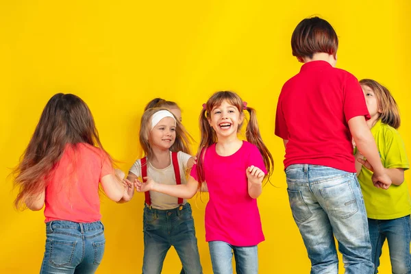 Crianças felizes brincando e se divertindo juntas no fundo do estúdio amarelo — Fotografia de Stock