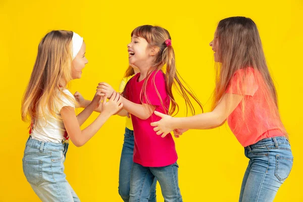 Crianças felizes brincando e se divertindo juntas no fundo do estúdio amarelo — Fotografia de Stock