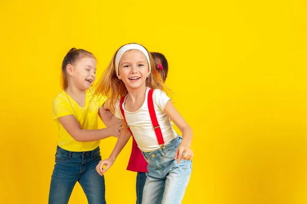 Happy children playing and having fun together on yellow studio background — ストック写真