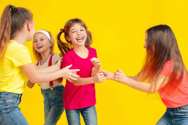 Crianças felizes brincando e se divertindo juntas no fundo do estúdio amarelo — Fotografia de Stock