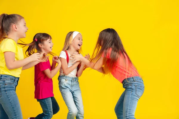 Bambini felici che giocano e si divertono insieme sullo sfondo giallo dello studio — Foto Stock