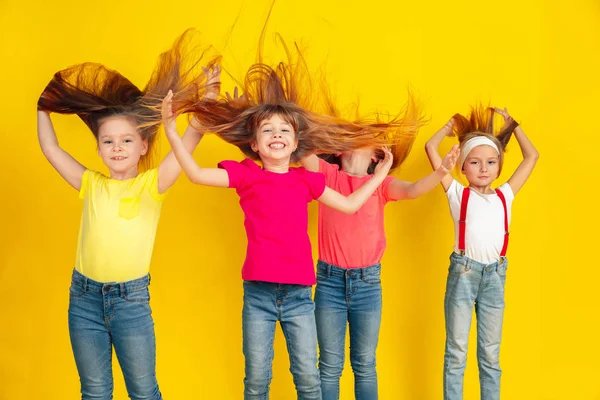 Niños felices jugando y divirtiéndose juntos en el fondo amarillo del estudio — Foto de Stock