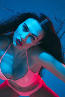 Attractive brunette model on blue studio background in neon light
