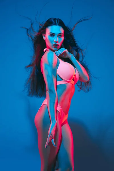Attractive brunette model on blue studio background in neon light — Stockfoto