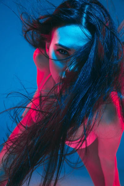Привлекательная модель брюнетки на синем фоне студии в неоновом свете — стоковое фото