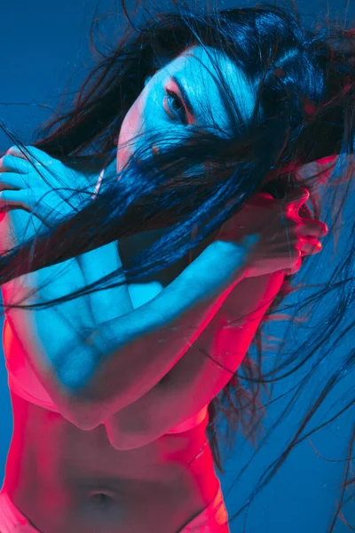 Attractive brunette model on blue studio background in neon light — Stock fotografie