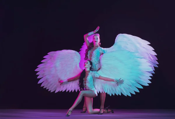 Fiatal női táncosok angyalszárnyakkal neon fény fekete háttér — Stock Fotó