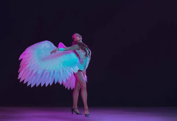Genç bayan dansçı meleklerin kanatlarıyla siyah arka planda neon ışığı — Stok fotoğraf