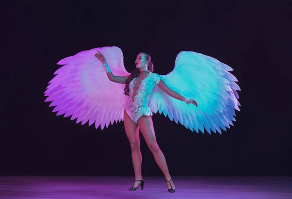 Young female dancer with angels wings in neon light on black background — Stock Photo, Image
