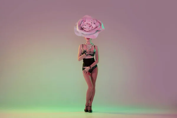 Young female dancer with huge floral hats in neon light on gradient background — 图库照片