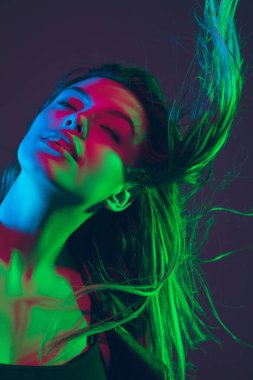 Güzel kadın portresi. Stüdyonun arka planında koyu renk neon ışıklarıyla saç üflüyor.