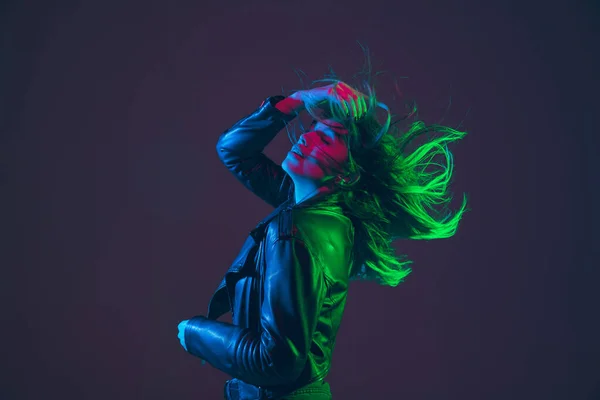 Gambar wanita cantik dengan rambut bertiup di latar belakang studio gelap dalam warna-warni cahaya neon — Stok Foto