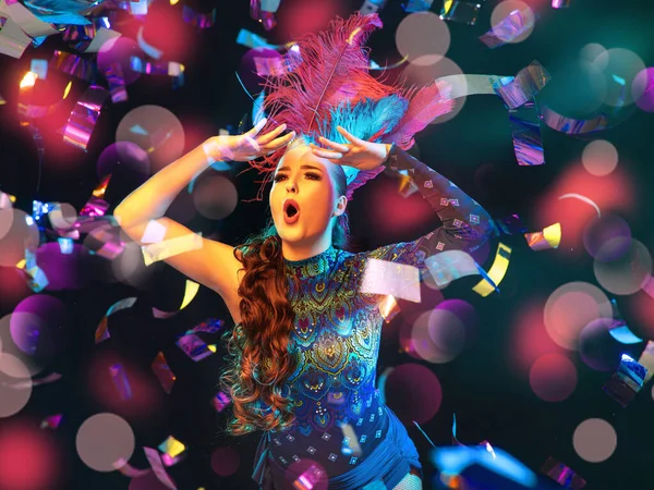 Wanita muda cantik di karnaval dan kostum topeng dengan lampu neon berwarna-warni dengan latar belakang hitam dengan taburan kertas terbang — Stok Foto